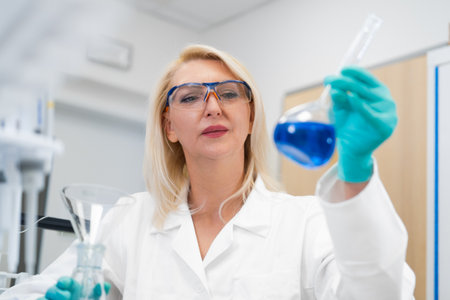 Middle aged female scientist watching chemical solution in glass flask in laboratory