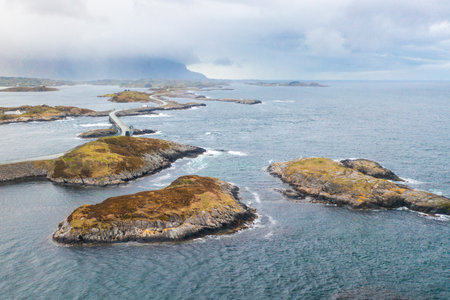 Curving bridges of the Atlantic Ocean Road stretch across small rocky islands, connecting Norways dramatic coastal landscape under cloudy skies.の写真素材