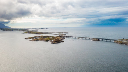 Magnificent stretch of Atlantic ocean road with long bridge gracefully spanning deep blue waters. Rough waves crash near rugged coastline in Norwayの写真素材