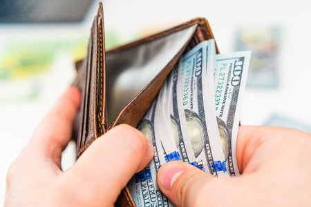 Man placing dollar banknotes into leather wallet. Cash payment, salary income, savings and financial...