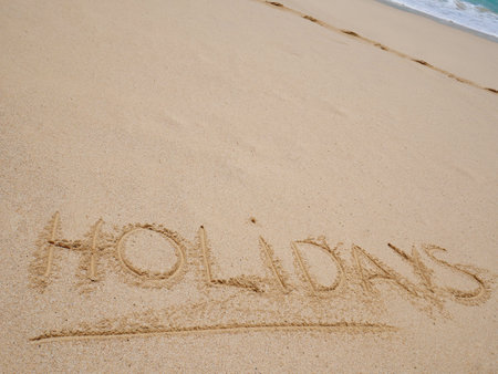 Closeup of word holidays written on the sand on beach and blue summer sky. Panoramic beach landscape. Empty tropical beach and seascape. Orange and golden sunset sky.の写真素材