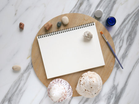 Open white note book on a wooden table, white background with seashells. Creativity products and blank note pad on stone background. Top view.の写真素材