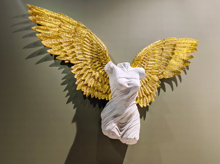 White marble statue of a woman angel from a stone with golden wings on a wall.
