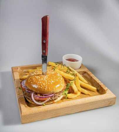 Tasty Hamburger Pierced With A Knife With French Fries And Ketchup On A Wooden Plateの写真素材