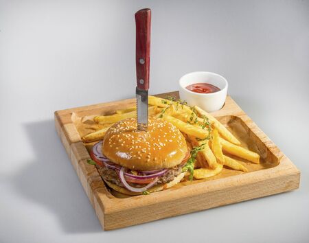Tasty Hamburger Pierced With A Knife With French Fries And Ketchup On A Wooden Plateの写真素材