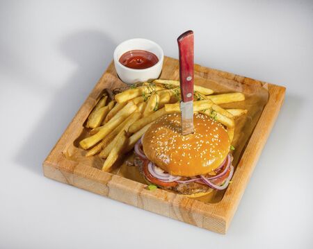 Tasty Hamburger Pierced With A Knife With French Fries And Ketchup On A Wooden Plateの写真素材