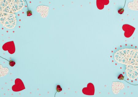 Valentine's Day blue background with rattan and felt hearts, red roses and small red and pink hearts. Greeting, invitation card. Wedding, love, happiness concept. Flat lay, top view with copy space.の写真素材
