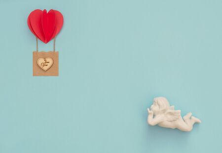 Valentine's Day blue background with white Cupid and red heart balloon with craft basket with wooden...
