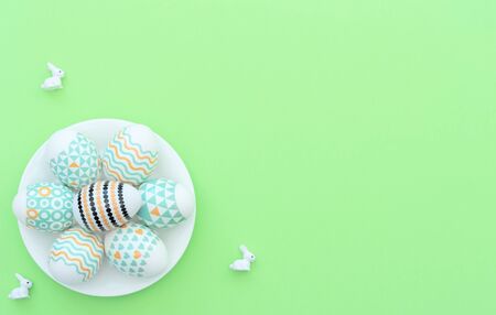 Decorated Easter egg lie on the white plate on green background with small bunnies. Happy Easter...