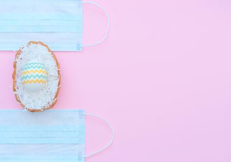 Decorated Easter egg in the basket and medical face masks on the pink background. Happy Easter during coronavirus, quarantine, stay home, social distance, COVID-19 concepts. Flat lay with copy spaceの写真素材