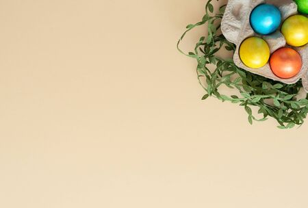 Decorated Easter eggs lie in the carton box on yellow background with green leaves. Happy Easter holiday and spring concept. Greeting, invitation card. Flat lay style with copy space.の写真素材