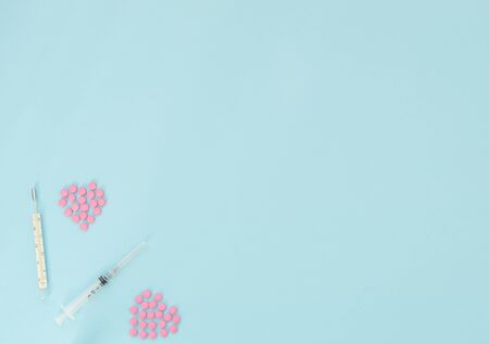 Two hearts made of pink pills, thermometer, syringe on light blue background. Seasonal diseases. Medicine concept. Flat lay style with copy space, top view.の写真素材