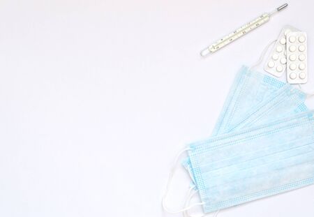 Blue medical masks, thermometer and white pills on white background. Seasonal diseases. Medicine concept. Flat lay style with copy space, top view.の写真素材