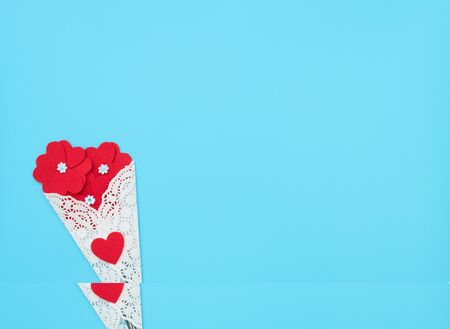 The flowers made of felt hearts wrapped in a white lace bundle on blue background with small white flowers. Mother's day, Valentine's day, Wedding, Birthday concept. Greeting card. Flat lay style.の写真素材