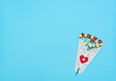 The bouquet of craft flowers wrapped in a white lace bundle on blue background with small yellow beads. Mothers day, Valentines day, Wedding, Birthday concept. Greeting card. Flat lay style.の写真素材