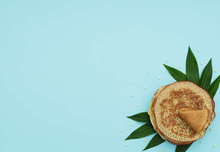 Homemade pancakes on blue background with green leaves and beads. Maslenitsa, spring festival concept. Russian traditional food. Pancake week. Delicious breakfast. Flat lay style with copy space.の写真素材