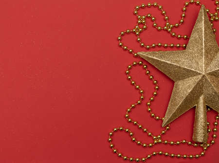 Christmas red background with golden star - the top of Christmas tree and golden beads. Flat lay...