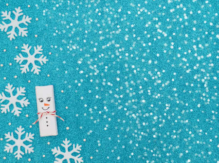 Christmas snowman with snowflakes and beads on blue background with white snow. New Year greeting...
