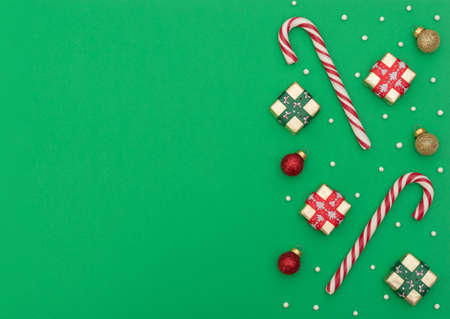 Two Christmas canes with gift boxes, red and gold Xmas balls and beads on green background. New Year greeting card. Christmas, New Year concept. Flat lay style with copy space.の写真素材