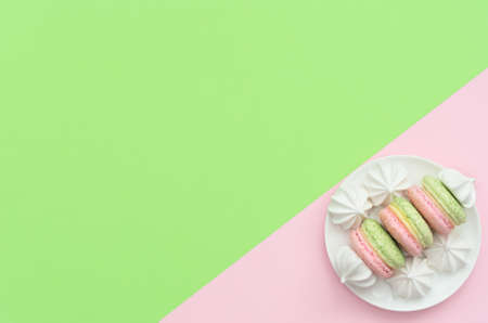 Delicious macarons with white merengues on white plate on double green and pink background. Happy day, breakfast, good morning concepts. Greeting or invitation card. Flat lay style with copy space.の写真素材