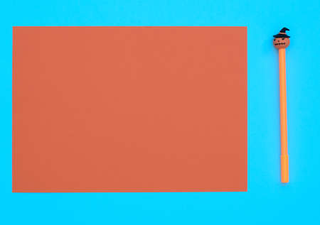 Orange pen with decorative pumpkin on blue background with orange sheet for your text. Halloween concept. Flat lay style with copy space.の写真素材