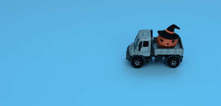 The gray truck car is carrying an orange decorative pumpkin on blue background. Halloween, minimalism concept. Greeting, invitation card. Wide banner for copy space.の写真素材