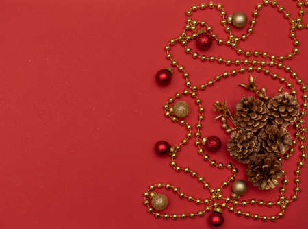 Christmas red background with fir cones, golden beads and Christmas decoration. Flat lay style. New Year greeting card.の写真素材