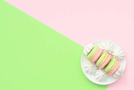 Delicious macarons with white merengues on white plate on double green and pink background. Happy day, breakfast, good morning concepts. Greeting or invitation card. Flat lay style with copy space.の写真素材