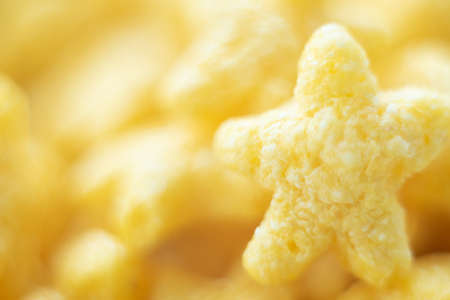 Abstract unfocused yellow background with macro of star-shaped corn flake. Close up image. Soft...