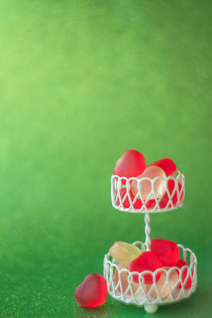 Red and white jelly hearts in white stand on blurred green background. Selective focus. Food macro,...