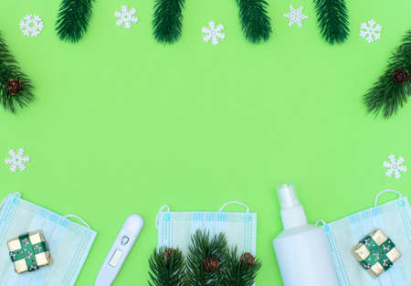 Christmas gifts, spruce with pine cones, medical face masks, thermometer, sanitizer on green...