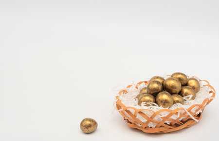 Golden chocolate Easter eggs in egg basket with white paper like a nest. Happy Easter holiday concept. Banner with copy space.の写真素材