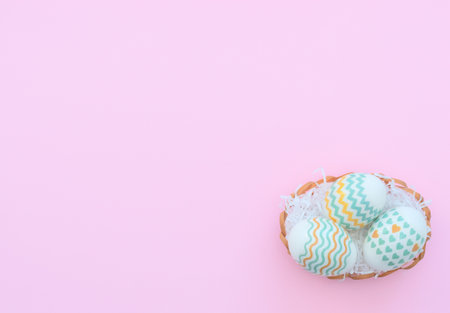 Decorated Easter eggs lie in the basket on pink background. Happy Easter holiday concept. Greeting, invitation card. Flat lay style with copy space.の写真素材