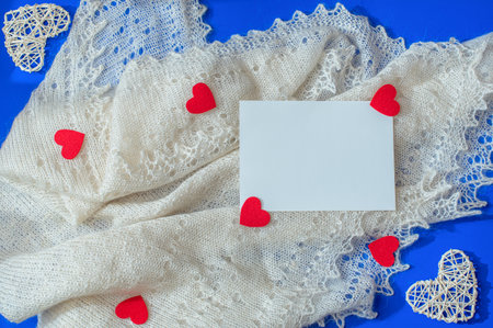 Love scene with white shawl, rattan and felt red hearts, paper card note on blue background. Valentine concept. Flat lay style with copy space.の写真素材