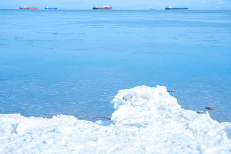 Winter scene with snow and blue sea against defocused background with ships. Landscape picture. Selective focus.の写真素材