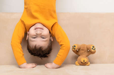 Child and teddy bear stand on their heads on the couch. A different view, childhood concept.の写真素材