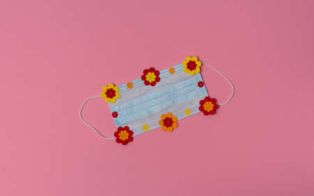 Medical protective face mask with bright paper flowers on pink background. Summertime during...