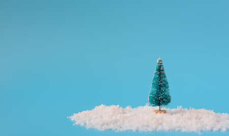 Christmas tree stands on white snow on blue background. Greeting or invitation card. Holiday minimalism conceptの写真素材
