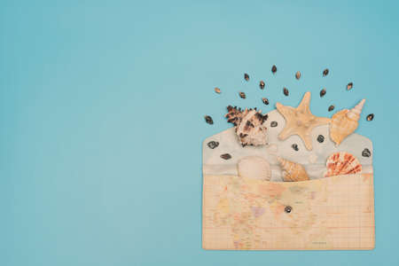 Different sea shells and starfish lay in opened envelope with map print on it on blue background....