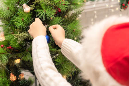 Child boy in red Santa hat decorates Christmas tree close up. Xmas or New Year cozy holidays concept. Selective focusの写真素材