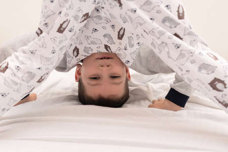 Child boy standing upside down and showing tongue on his bed at the morning. Morning exercises....
