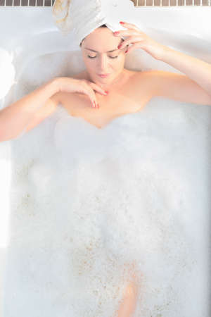 Young woman takes a bath with lush foam near the window. Personal hygiene, healthcare concept