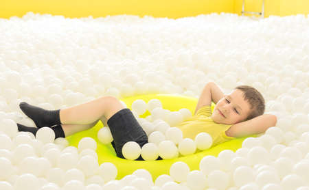 Child boy lying with closed eyes in yellow inflatable swimming ring in the big dry pool with...
