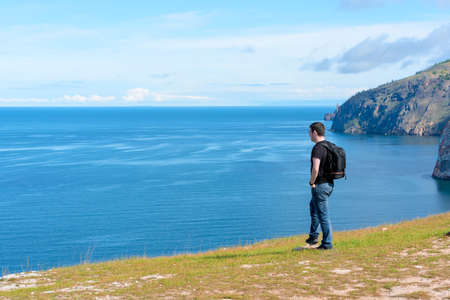 Man with backpack standing on a rock at the end of earth watching on the bright blue lake. Hiking or travel concept. Exploring the great outdoors. Beauty of natureの写真素材