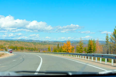Bright autumn scene with road among orange and green trees and blue sky. Soft selective focus....