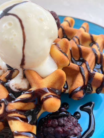 Belgian waffles with scoop of ice cream, fresh berries and chocolate topping on blue plate close up. Food background with selective focusの写真素材