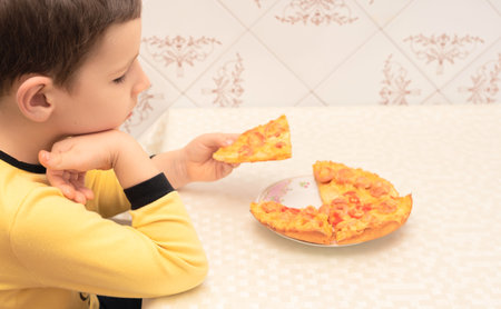 Child are going to eat homemade pizza with sausages, tomatoes and cheese sitting at the table in the kitchen close up with selective focus.の写真素材