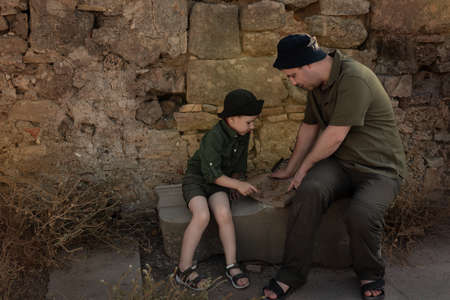 Two archeologists, child and adult, in khaki clothes sitting on ruins and studying an ancient map. Diverse, non-traditional job conceptの写真素材