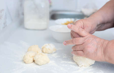 Senior woman hands kneading dough on a white kitchen table with blurred grated apple and sugar on...