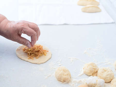 Senior woman hands put the apple filling on the dough for pies on a white kitchen table. Selective focus. Process of making pies with apple filling. Cooking at home concept. Tradition home-made foodの写真素材